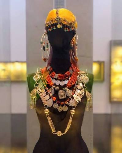A museum display of traditional Moroccan-Jewish jewelry — an elaborate headdress and necklace assemblage combining silver, coral, amber and enamel in the distinctive style developed by Jewish craftsmen in Morocco over centuries, now preserved in a museum collection